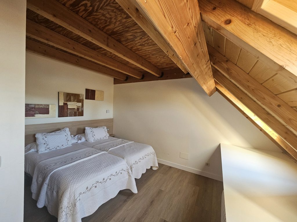Dormitorio de dos camas con techo aboardillado en madera