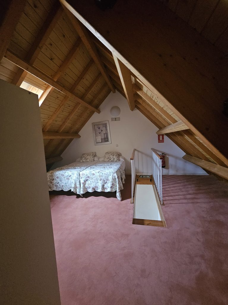 Vista de conjunto, al fondo dos camas y la escalera, techo en madera aboardillado a dos aguas